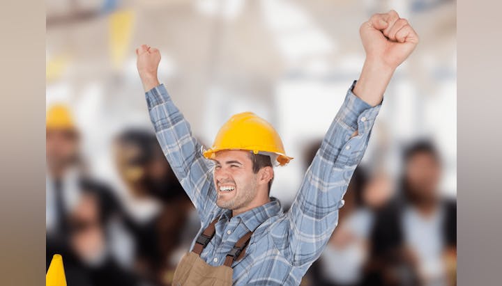 Joyful construction worker celebrating with raised fists, wearing a yellow hard hat, plaid shirt, and tool belt.