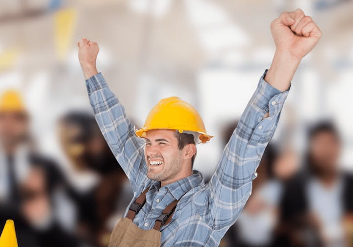 Joyful construction worker celebrating with raised fists, wearing a yellow hard hat, plaid shirt, and tool belt.