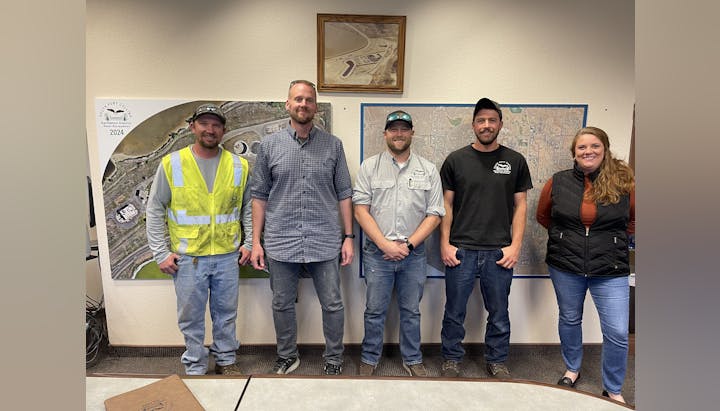 Five people standing in front of maps, some wearing casual clothing, one in a safety vest.