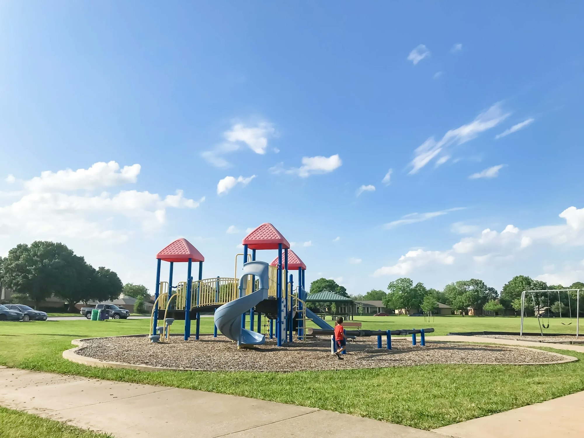 A vibrant playground with slides, swings, and a child, under a clear blue sky.