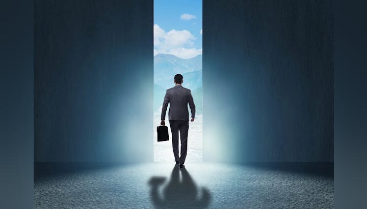 Man with briefcase walking towards mountains through a large split in a wall.