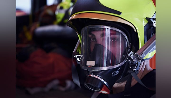 Close-up of a person wearing a firefighter helmet and mask.