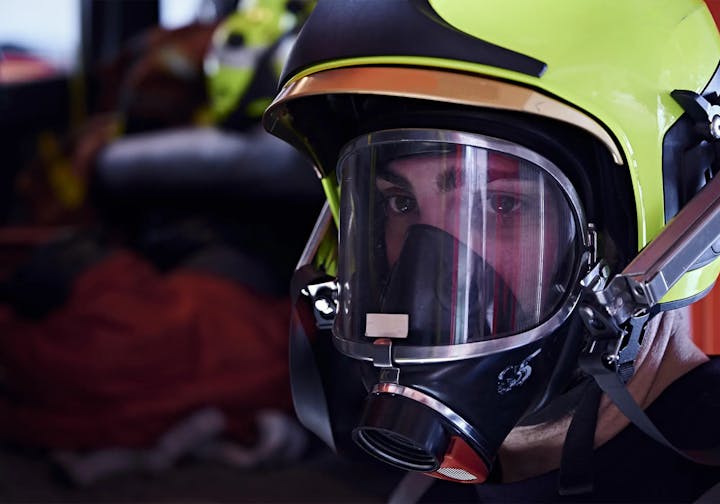 Close-up of a person wearing a firefighter helmet and mask.