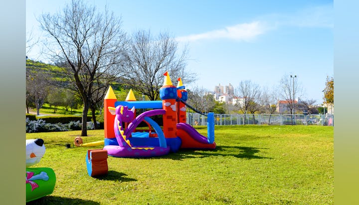 Inflatable bounce castle in a park on a sunny day with trees and buildings in the background.