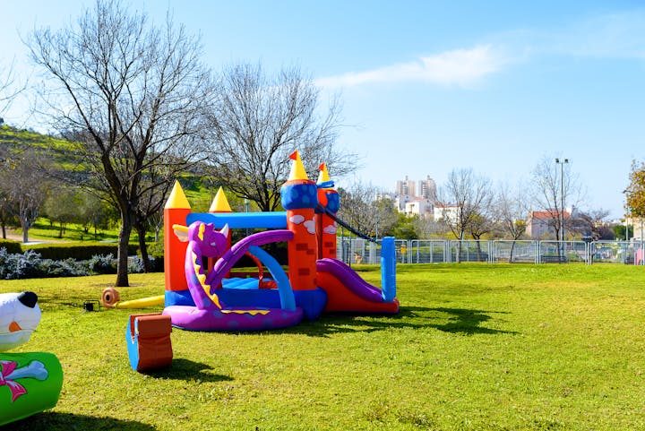 Inflatable bounce castle in a park on a sunny day with trees and buildings in the background.