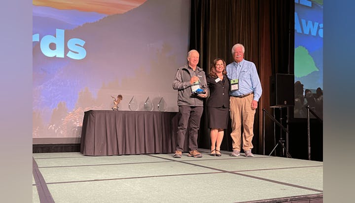 Three people on a stage at an awards ceremony with a backdrop that reads "Awards."