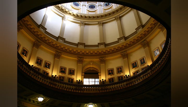 An ornate interior dome with portraits and people on the balcony.
