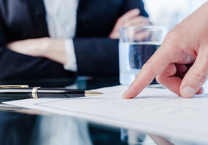 A person pointing at a document, pen nearby, suggesting a business meeting or contract signing.