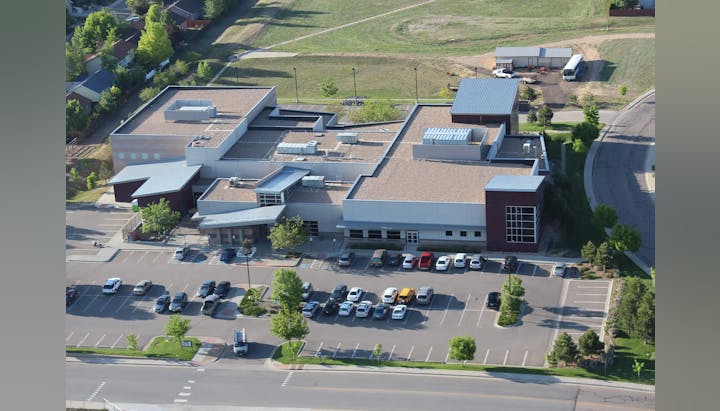Aerial view of a modern building with a parking lot and green areas.