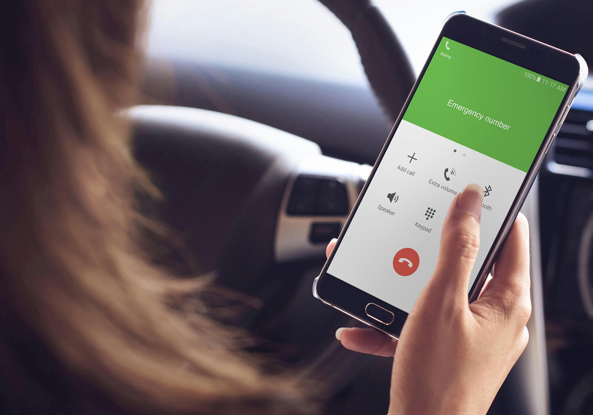 A person is dialing an emergency number on a smartphone in a car.