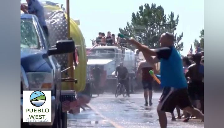A water fight with people using squirt guns, a firetruck spraying water, and a crowd having fun.