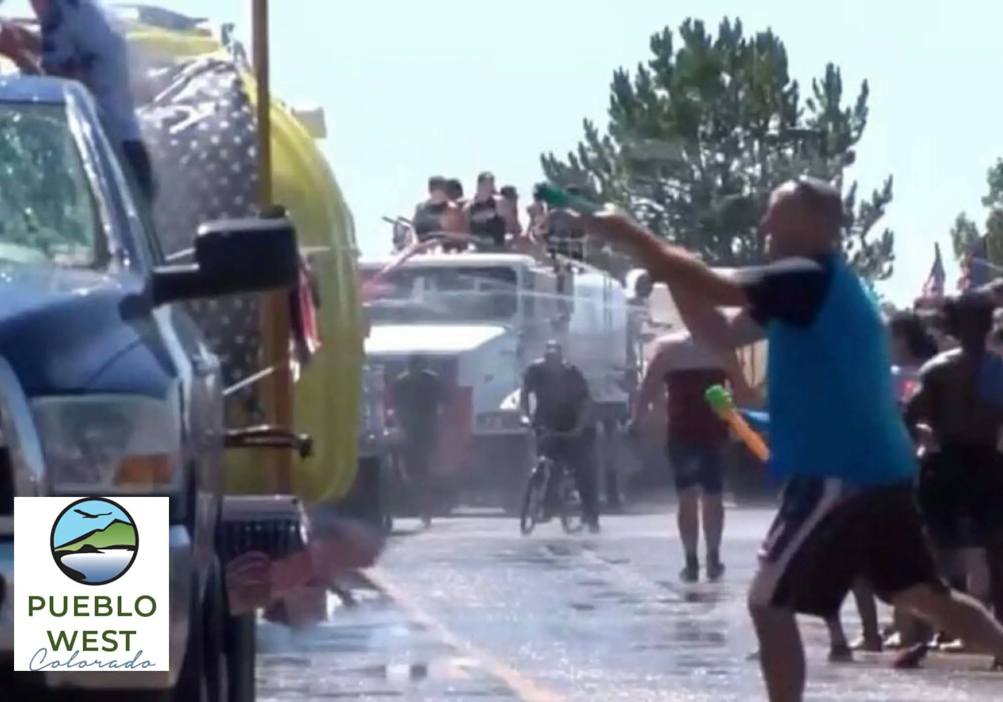 A water fight with people using squirt guns, a firetruck spraying water, and a crowd having fun.