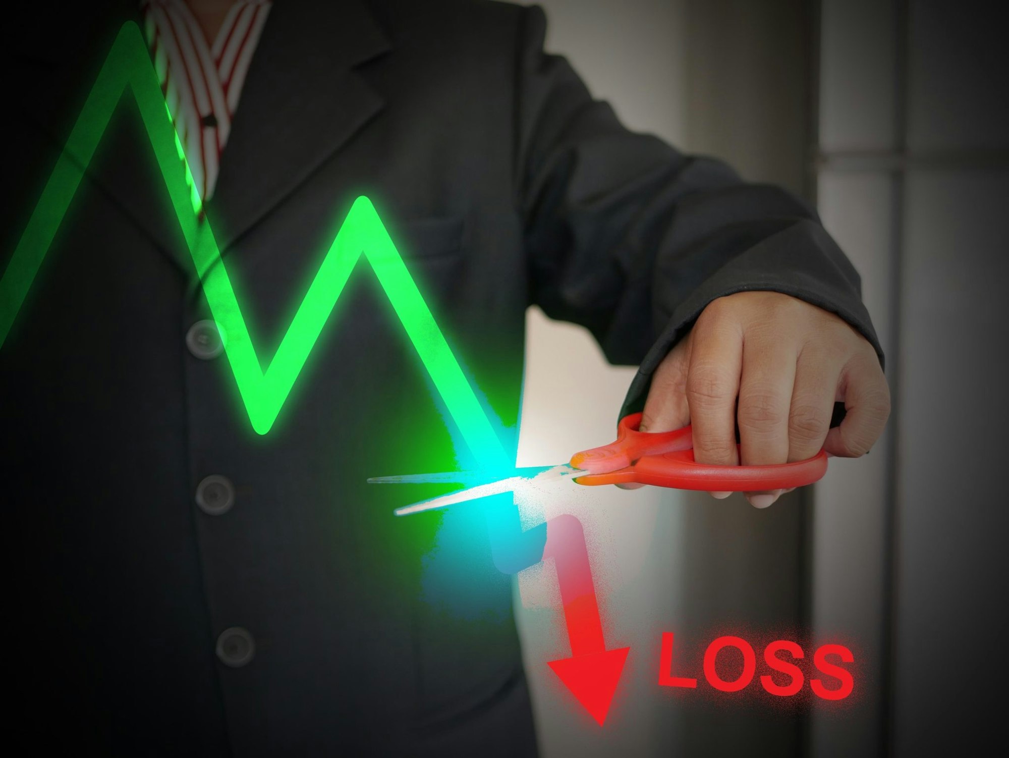 A person in a suit cutting a declining graph line with scissors, indicating financial loss.
