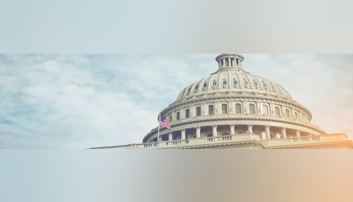 The United States Capitol building with an American flag, under a bright sky.