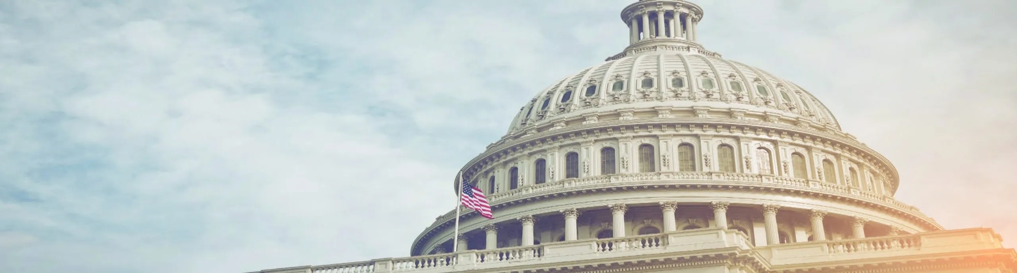 The United States Capitol building with an American flag, under a bright sky.