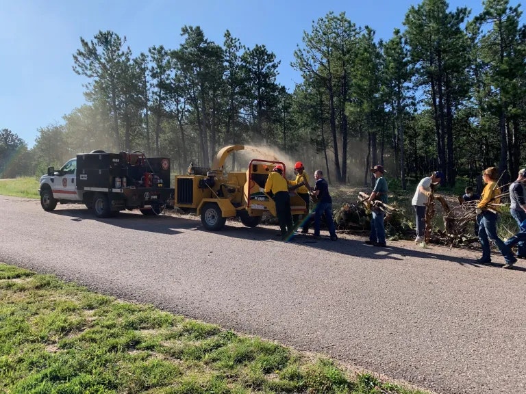People working outdoors with a wood chipper and a truck on a sunny day.