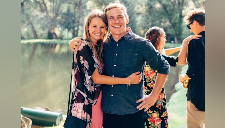 A smiling man and woman embracing at an outdoor gathering.