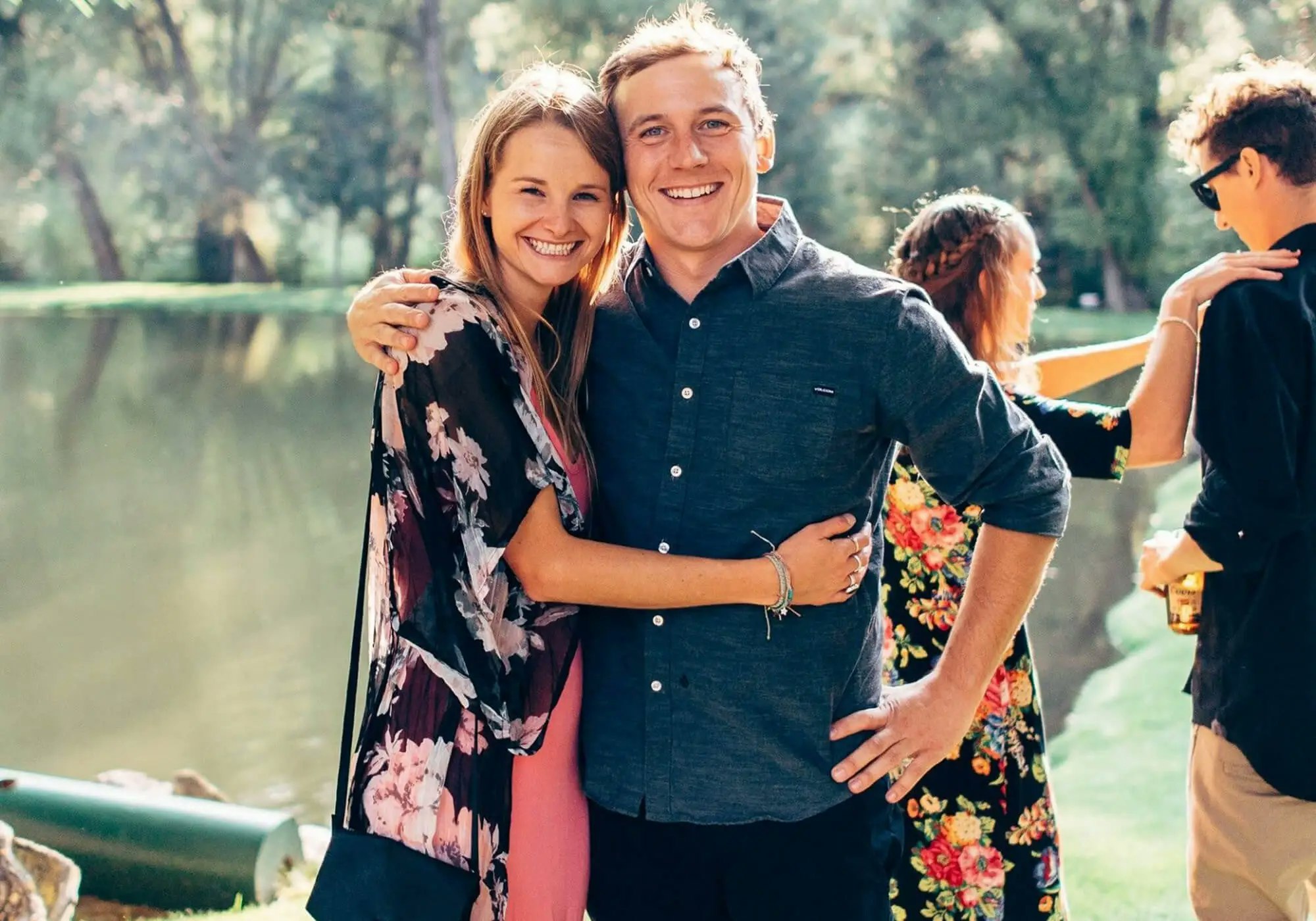 A smiling man and woman embracing at an outdoor gathering.