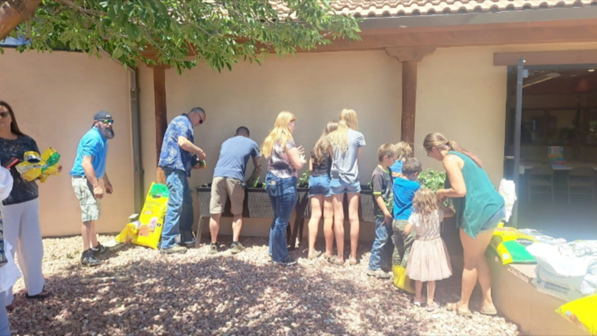 Group of people, including children, engaging in an outdoor activity, possibly a community or gardening event.