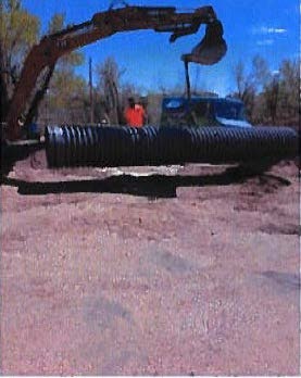An excavator with a large pipe, possibly at a construction site.