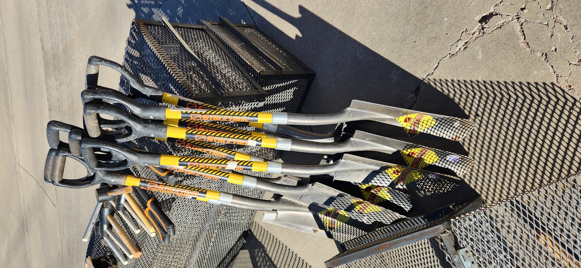 Assorted firefighter tools on textured ground, with prominent shadows.