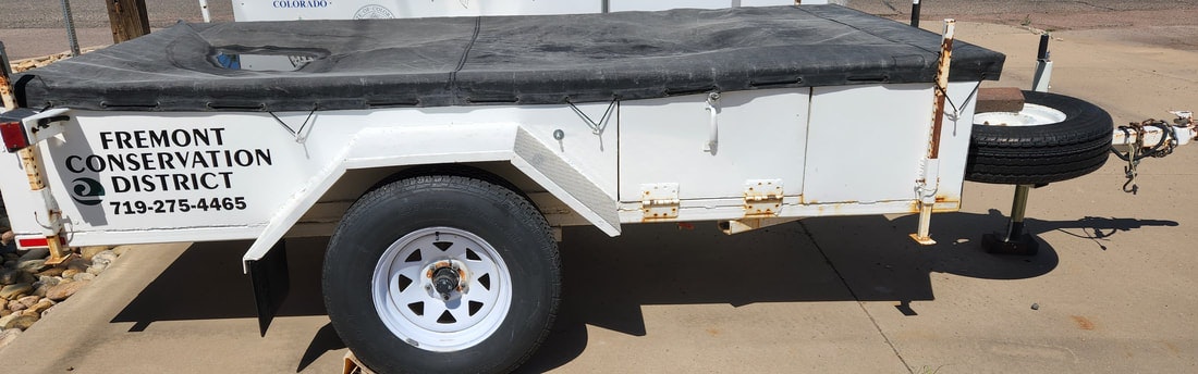 A trailer from the Fremont Conservation District, featuring a black cover and a spare tire attached.