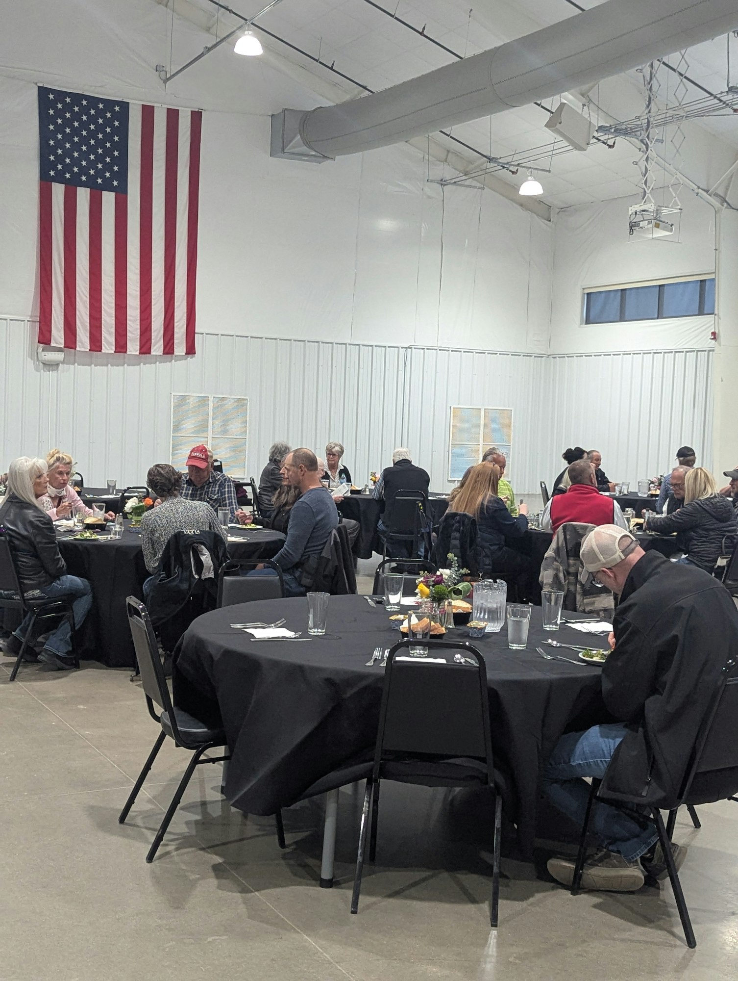 People seated at round tables in a large room with an American flag on the wall.