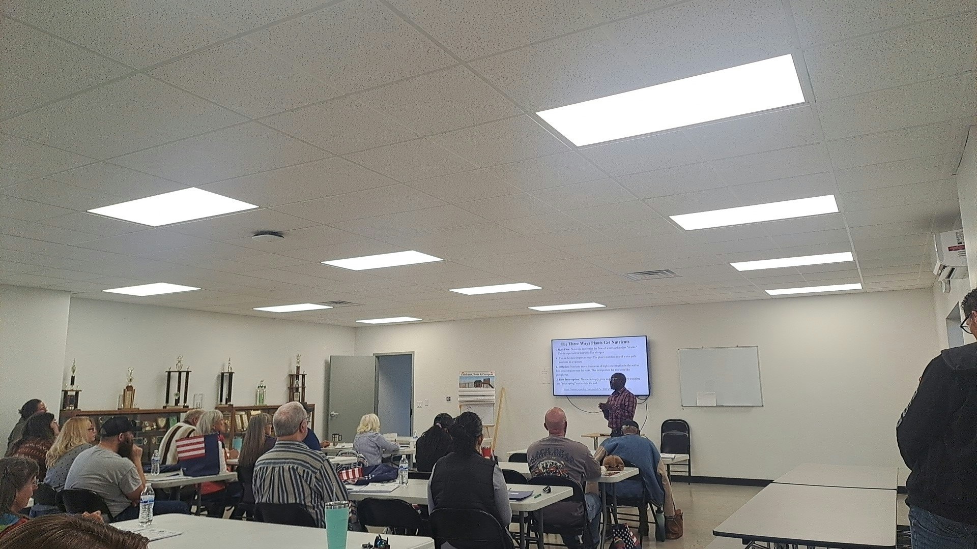 A presentation session in a classroom with attendees listening and a screen displaying information about plant nutrition.