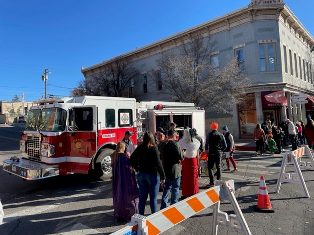 A fire truck parked on a street with a group of people, some in costumes, and traffic cones indicating an event or emergency.