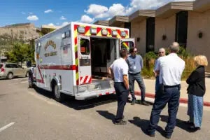 An ambulance with open doors and a group of people standing and talking near it.