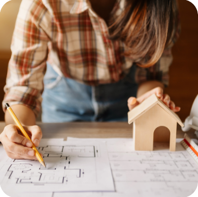 A person reviews blueprints with a miniature house model nearby, possibly planning or designing a home.