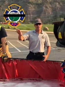 A man wearing sunglasses and a cap stands beside a helicopter, with a blurred emblem in the corner and scenic background.