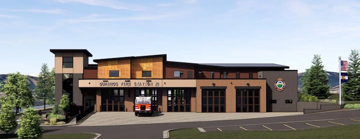 A modern fire station with an emergency vehicle, flags, and trees.