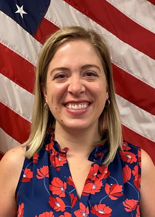 A woman smiling in front of the American flag.