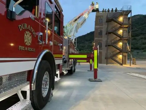 A fire truck with an extended ladder near a training tower at dusk.