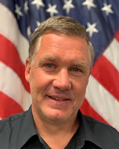 A man smiling in front of an American flag.