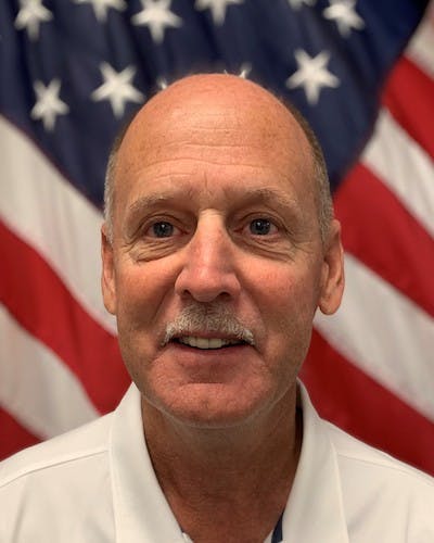 A man with a mustache in front of an American flag.
