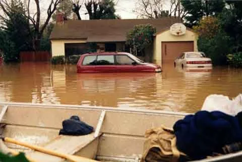 A flooded residential area with water submerging cars and a nearby boat.