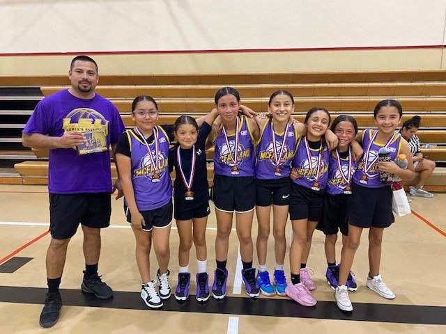 A basketball coach and team of young girls with medals, smiling in a gym.