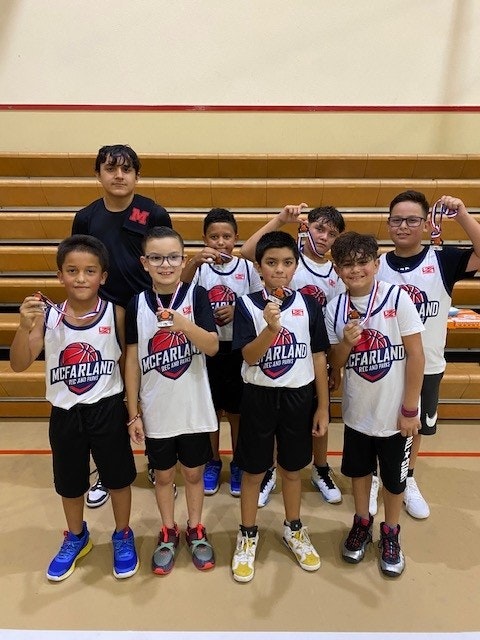 A youth basketball team posing with medals in a gym.