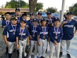 A youth baseball team wearing navy jerseys and hats, each with a medal, posing together outdoors.