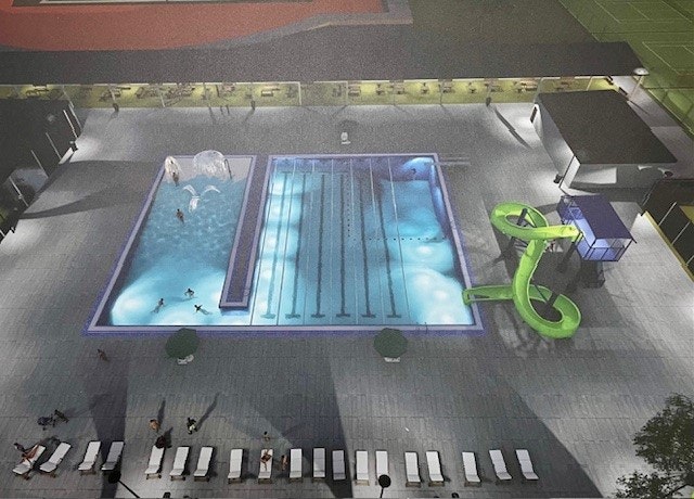 Aerial view of a swimming pool with lanes, a slide, people swimming, sunbathers, and surrounding walkways.