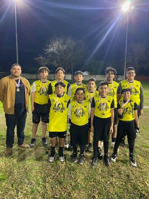 A soccer team with medals, a coach, and a night-time field backdrop.