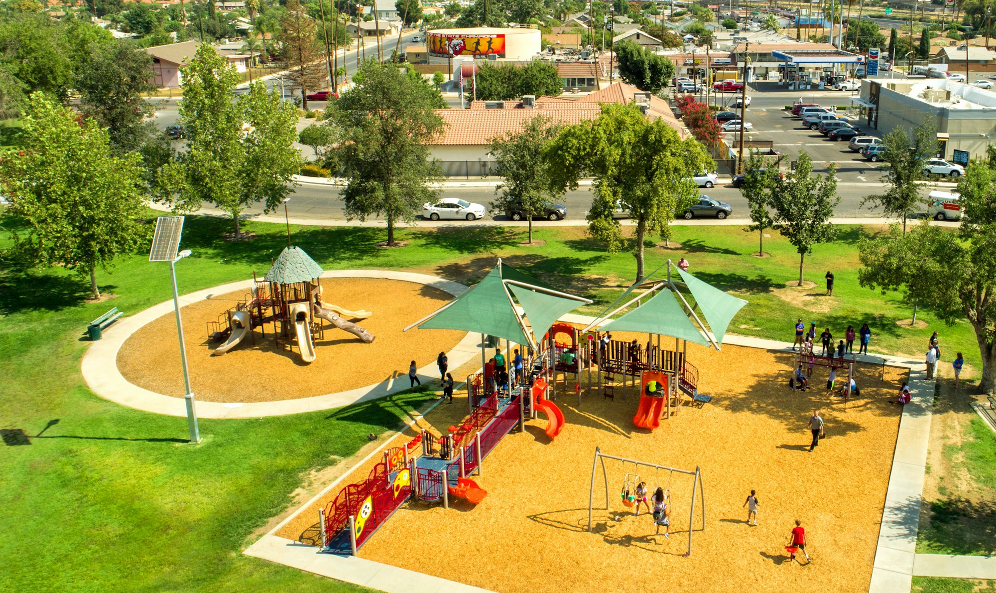 A vibrant playground with children playing, surrounded by green trees and a sunny, urban backdrop.
