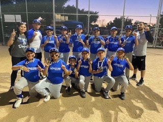 A youth baseball team in blue uniforms poses with trophies on a field.