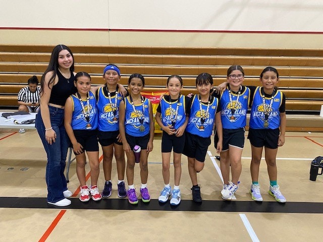 A group of young basketball players with medals and their coach posing in a gym.
