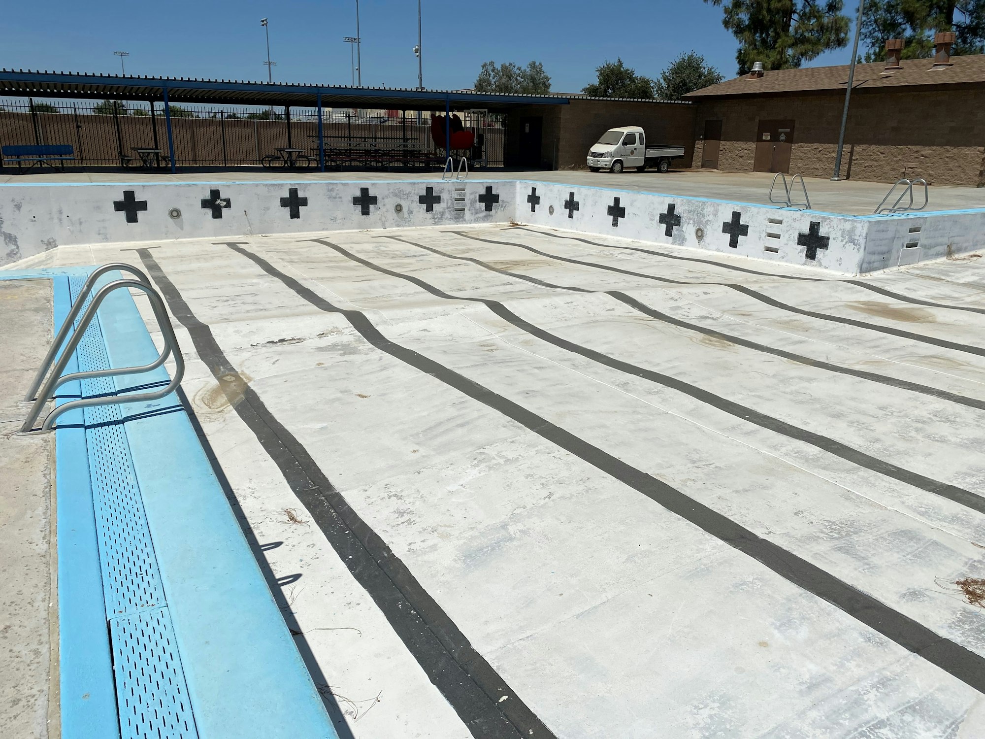 An empty outdoor swimming pool with marked lanes and starting blocks, under a clear sky.
