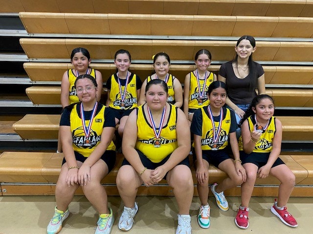 A group of young basketball players with medals and their coach sitting in the bleachers.