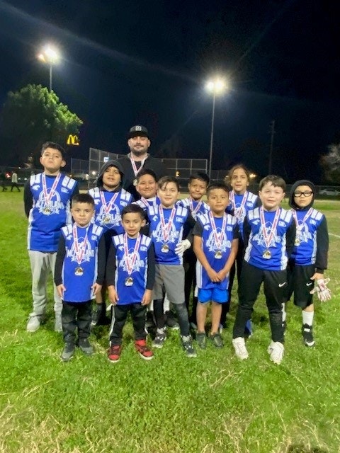 A group of young soccer players with medals and their coach, standing on a field at night.