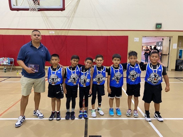A basketball team of young players with medals, and a coach, indoors.